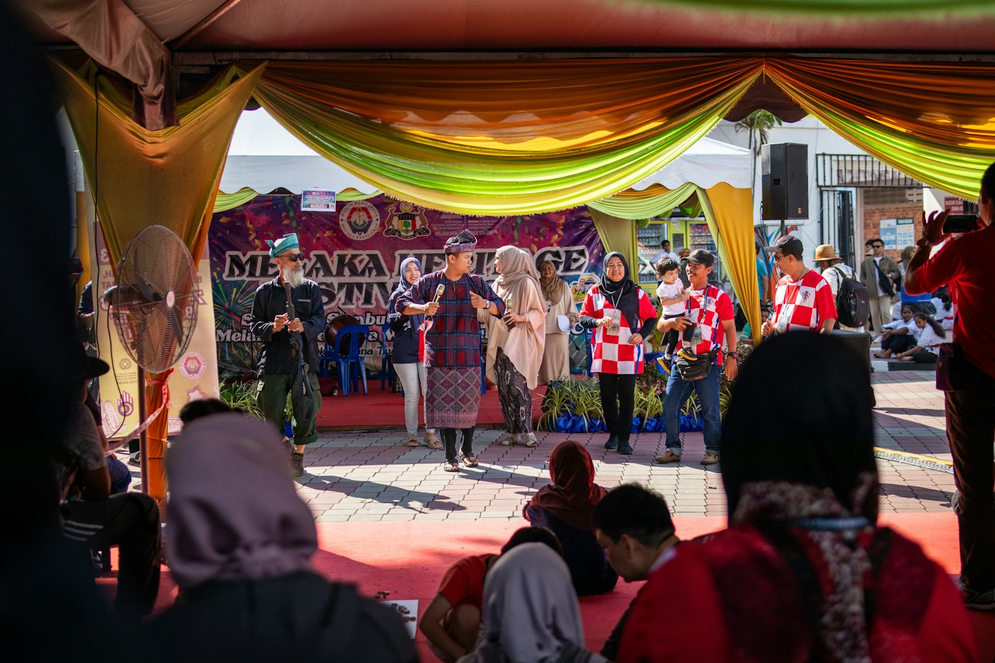 Persone su un palco con tappeto rosso che parlano a una festa di comunità.
